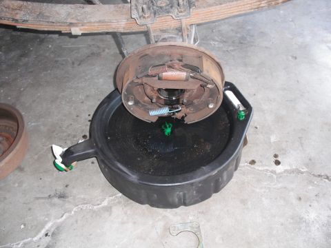 1991 Ford Bronco - A rear axle brake drum assembly is shown positioned over a black oil drain pan, likely during maintenance.