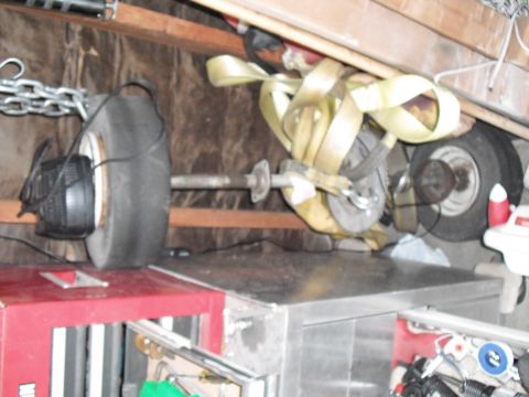 1991 Ford Bronco - Tire and axle assembly with tie-down straps and chain, stored indoors.