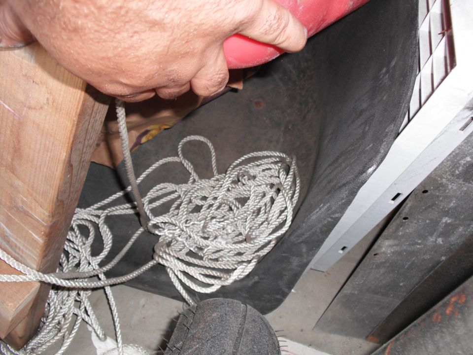 Coiled rope and wooden beam in a dark area, with a tire visible at the bottom