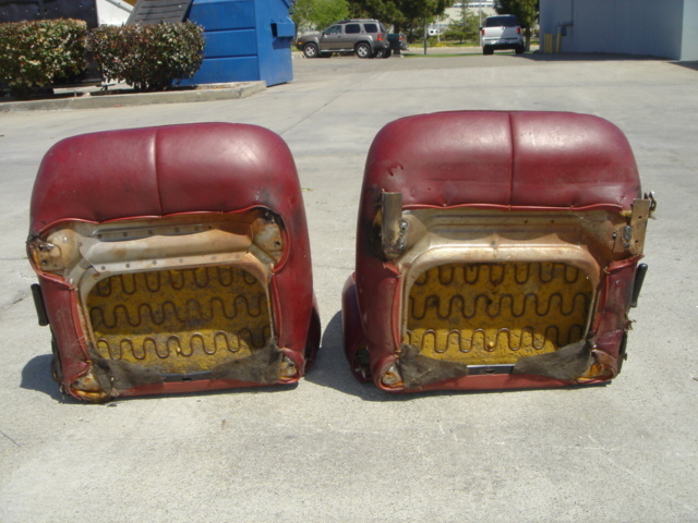 Two red car seats with exposed springs and metal frames, viewed from the back