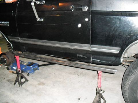 1991 Ford Bronco - A black 1991 Ford Bronco is shown from the side, elevated on jack stands with custom metal sliders installed.