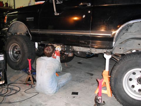 1991 Ford Bronco - A person works on the undercarriage of a black Ford Bronco, which is supported by jack stands in a garage.