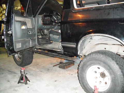 1991 Ford Bronco - Black Ford Bronco interior visible with driver's door open and vehicle on jack stands.