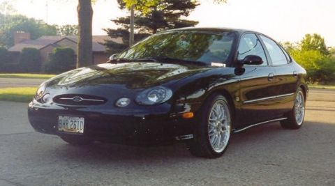 1999 Ford Taurus - A black 1999 Ford Taurus is parked outside a house on a sunny day.