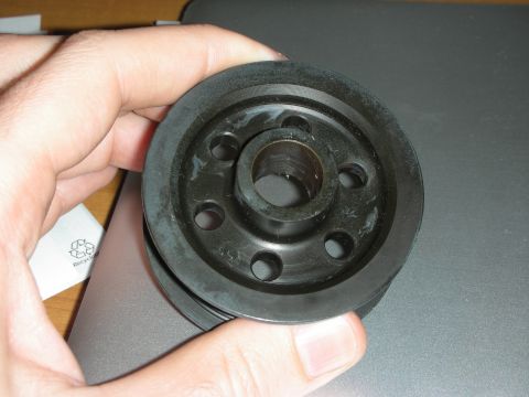 1998 Ford Crown Victoria - A person holds a black pulley, a component likely from a vehicle's engine system.