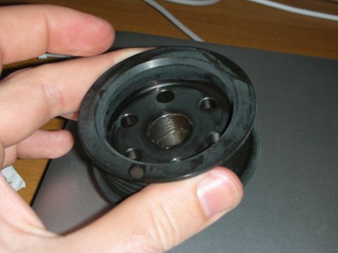 1998 Ford Crown Victoria - A black automotive pulley with a rubber seal is held in a person's hand.