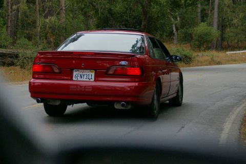 1990 Ford Taurus - Rear view of a red 1990 Ford Taurus on a scenic road.