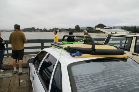 1990 Ford Taurus - A white sedan and a beige SUV are parked on a pier, with surfboards strapped to the sedan's roof.