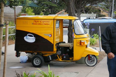 1990 Ford Taurus - A yellow three-wheeled auto rickshaw, branded "Moto Espresso - Mobile Coffee & Espresso", is parked on a sidewalk.