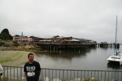 1990 Ford Taurus - A man stands on a pier overlooking a body of water with buildings and a sailboat.
