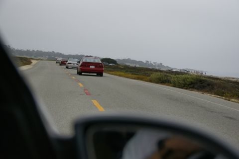 1990 Ford Taurus - Several cars drive along a scenic coastal highway under an overcast sky.