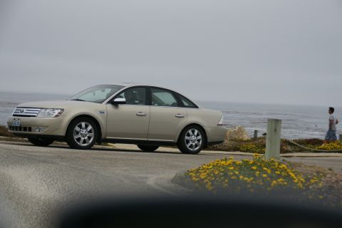 1990 Ford Taurus - A tan sedan is parked near the ocean on a cloudy day.