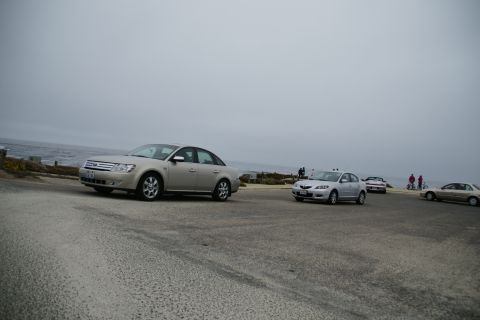 1990 Ford Taurus - Several cars parked near the coast on an overcast day, with the ocean in the background.