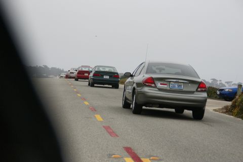 1990 Ford Taurus - A line of cars drives down a road on a foggy day, with a blue car visible on the right.