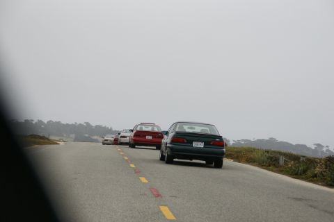 1990 Ford Taurus - Multiple vehicles drive along a coastal road under a hazy sky.