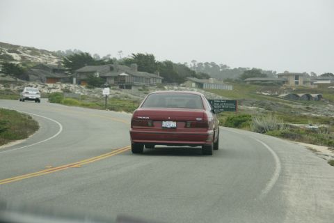 1990 Ford Taurus - Driving a 1990 Ford Taurus on a scenic coastal highway with other vehicles and homes visible.
