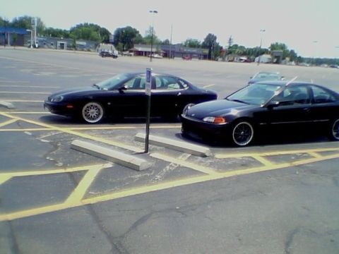 1999 Ford Taurus - Two black cars are parked in a lot on a sunny day.