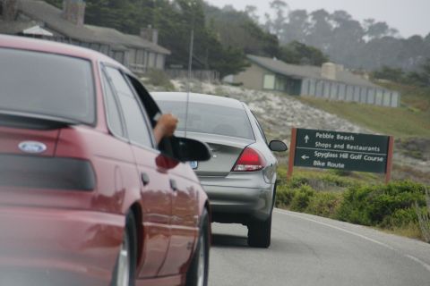 1990 Ford Taurus - A red 1990 Ford Taurus drives on a road near Pebble Beach, with a silver sedan following.