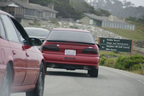 1990 Ford Taurus - Rear view of a red 1990 Ford Taurus driving on a road near Pebble Beach.