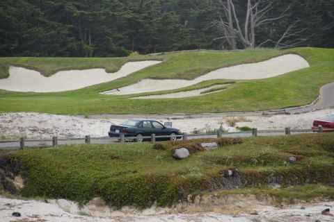 1990 Ford Taurus - A 1990 Ford Taurus sedan is seen parked near a golf course with sand traps and trees in the background.