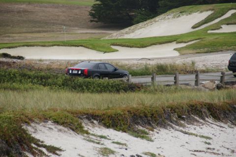 1990 Ford Taurus - A black sedan is parked on a road beside a golf course with sand traps and green grass.