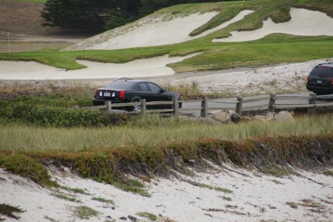 1990 Ford Taurus - A black sedan is parked on a road beside a golf course, with another vehicle partially visible on the right.