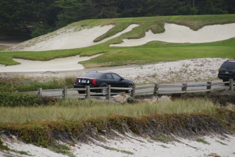 1990 Ford Taurus - A black sedan is parked on a road beside a golf course with sand traps and trees in the background.