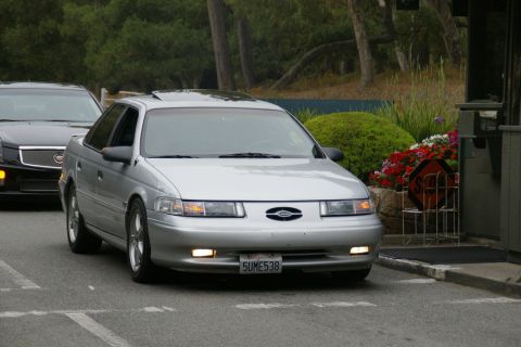 1990 Ford Taurus - A silver sedan is seen from the front, with another dark-colored vehicle behind it.