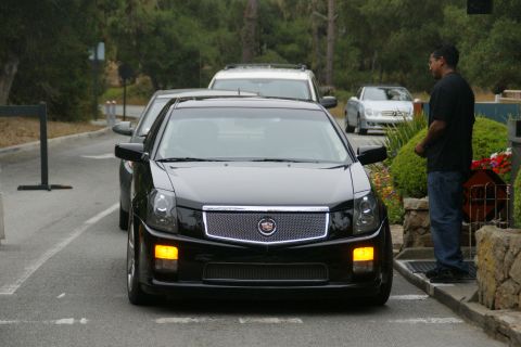 1990 Ford Taurus - A black Cadillac CTS is parked on the street, with a man standing to the right of the vehicle.