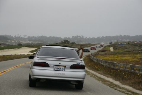 1990 Ford Taurus - Silver 1990 Ford Taurus driving on a road with other cars in a procession.
