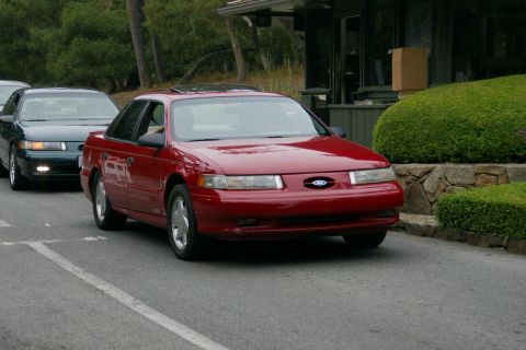 1990 Ford Taurus - A red Ford Taurus is seen driving, with another Taurus following closely behind on the road.