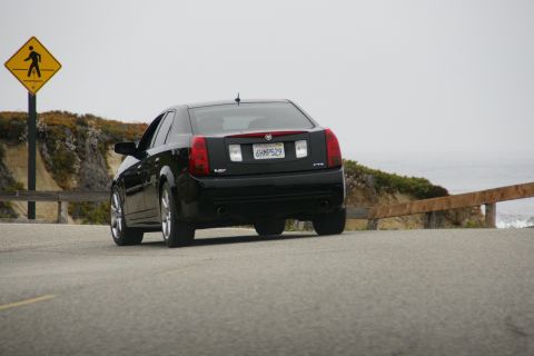 1990 Ford Taurus - Cadillac CTS-V seen on a coastal highway with a pedestrian crossing sign.