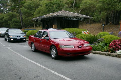 1990 Ford Taurus - A red Ford Taurus passes through the Pacific Grove Gate, with a dark green Taurus following closely behind.