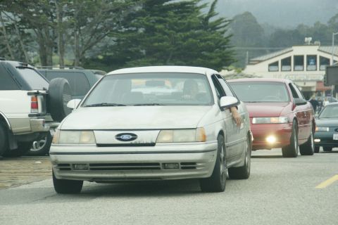 1990 Ford Taurus - A white 1990 Ford Taurus is seen from the front in a line of cars on a road.