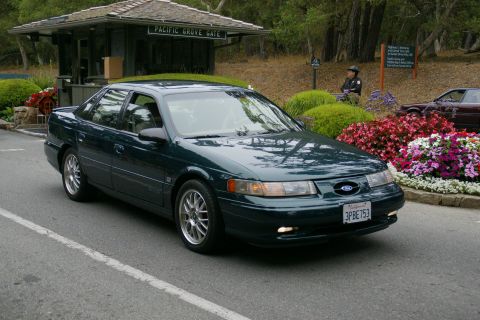 1990 Ford Taurus - A dark green sedan is seen near the Pacific Grove Gate, with a second car visible in the background.