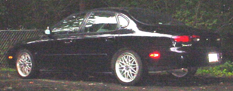 Black Ford Taurus sedan side-rear at night with lit taillights and silver wheels