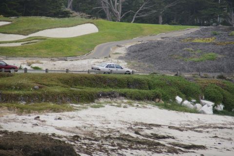 1990 Ford Taurus - A silver sedan drives along a coastal road with a golf course and beach scenery.