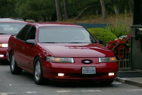 1990 Ford Taurus - A red sedan, possibly a 1995 Ford Taurus, is seen from the front with another red vehicle behind it.