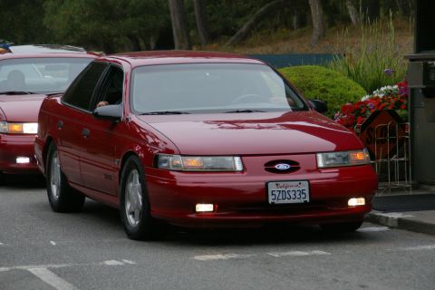 1990 Ford Taurus - A red Ford Taurus is seen from the front, with another red car behind it.
