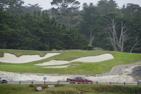 1990 Ford Taurus - A red sedan is seen driving on a road adjacent to a golf course with sand traps and trees in the background.