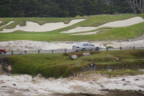 1990 Ford Taurus - A silver sedan drives along a coastal road with a golf course in the background.