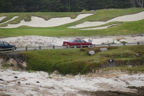 1990 Ford Taurus - A 1990 Ford Taurus drives past a golf course with sand traps and green fairways.