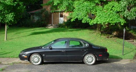 1999 Ford Taurus - Side view of a black 1999 Ford Taurus sedan parked on a residential street.