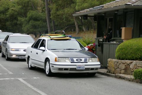 1990 Ford Taurus - A white 1990 Ford Taurus with surfboards on its roof is in line at a gatehouse.