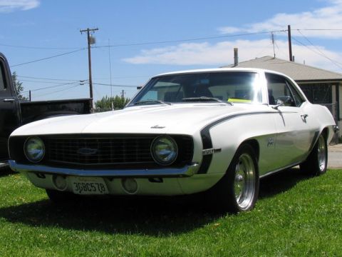 1984 Ford Bronco - A white 1969 Chevrolet Camaro with black racing stripes is parked on a grassy lawn under a blue sky.