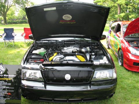 2003 Mercury Marauder - A black 2003 Mercury Marauder is displayed with its hood open, revealing the supercharged engine, alongside other vehicles at a car show.