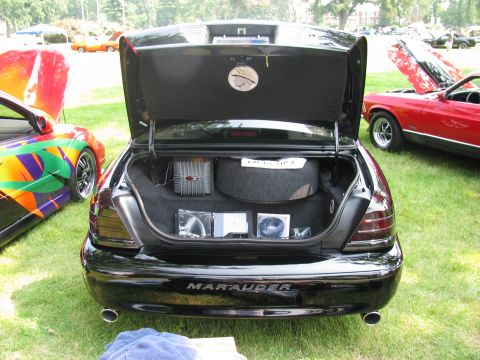 2003 Mercury Marauder - The trunk of a black Mercury Marauder is open, revealing a spare tire and audio equipment, with other vehicles in the background.