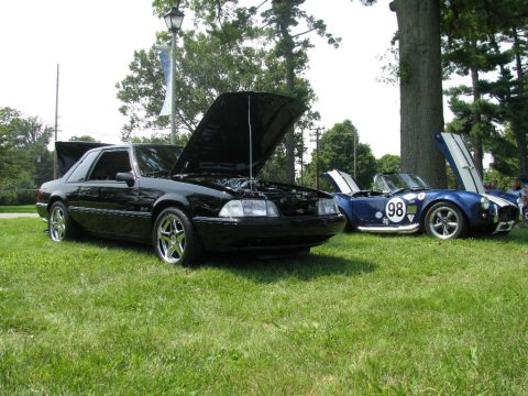 2003 Mercury Marauder - A black 1987 Ford Mustang coupe is parked on grass with its hood open, alongside another vehicle.
