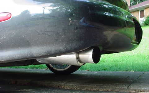 1999 Ford Taurus - Close-up of a car's rear bumper and exhaust system, with grass and a house in the background.