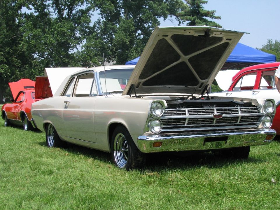 Cream-colored 1966 Ford Fairlane with hood open, parked on grass next to a red car